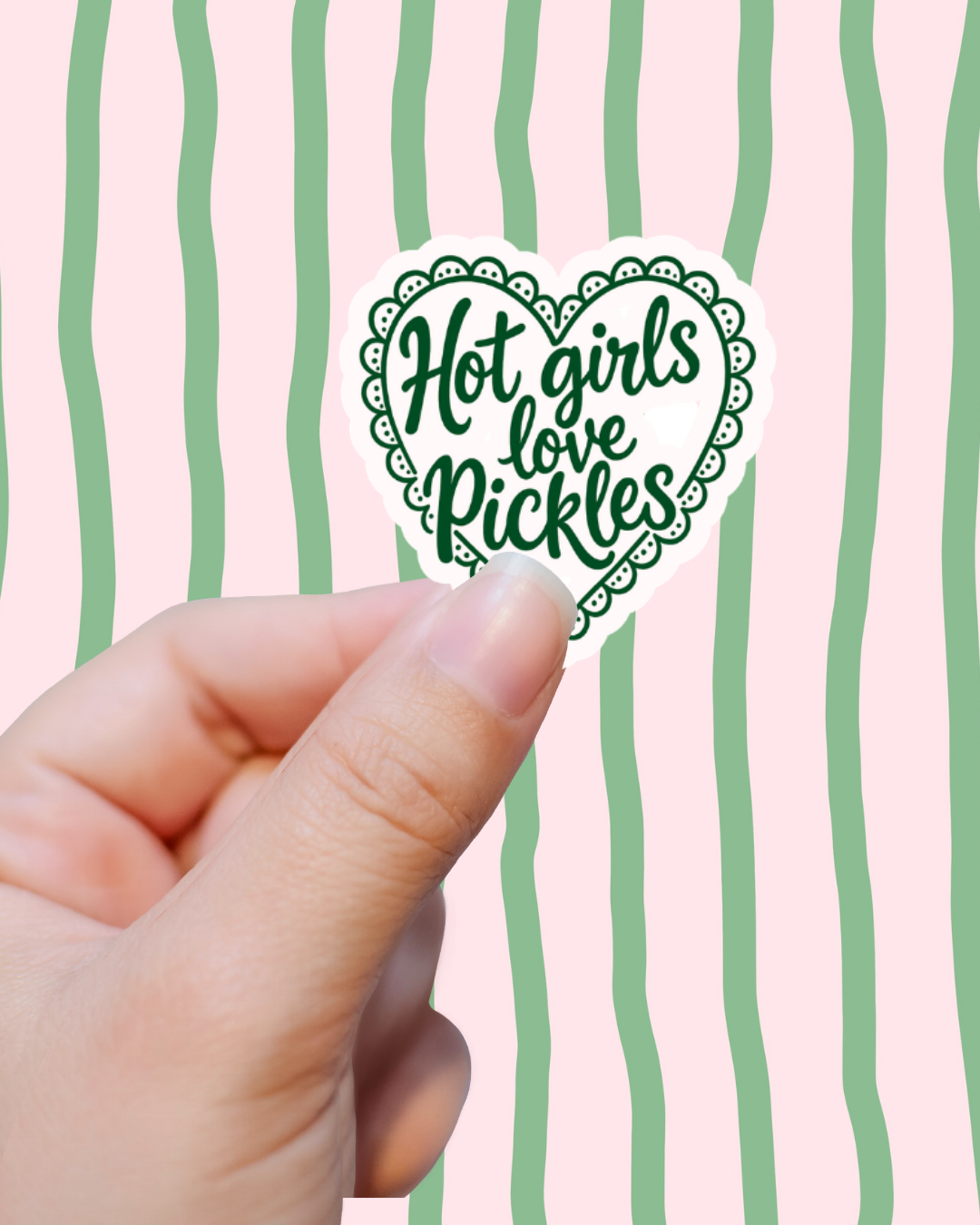 Hand holding a sticker with 'Hot girls love Pickles' text against a pink background with green stripes