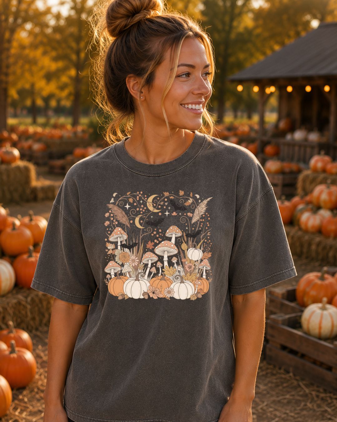 Woman wearing a dark charcoal Comfort Colors tee with a cottagecore mushroom, pumpkin, and crescent moon fall graphic at a pumpkin patch