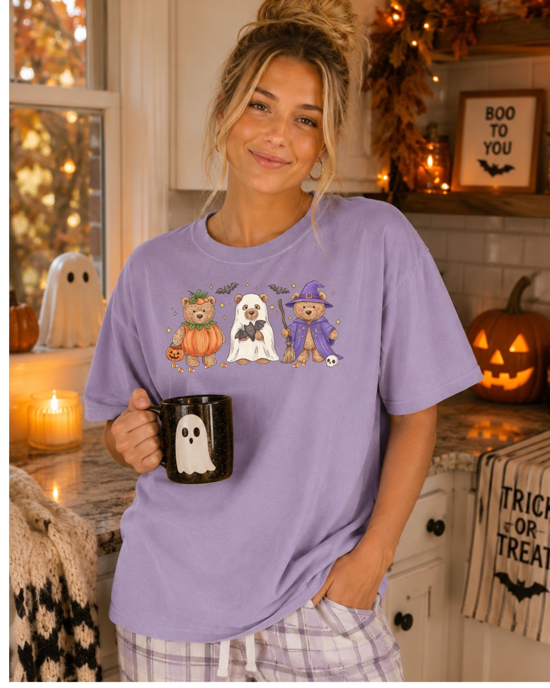 Woman wearing a lavender Comfort Colors tee with three Halloween teddy bears dressed as a pumpkin, ghost, and witch