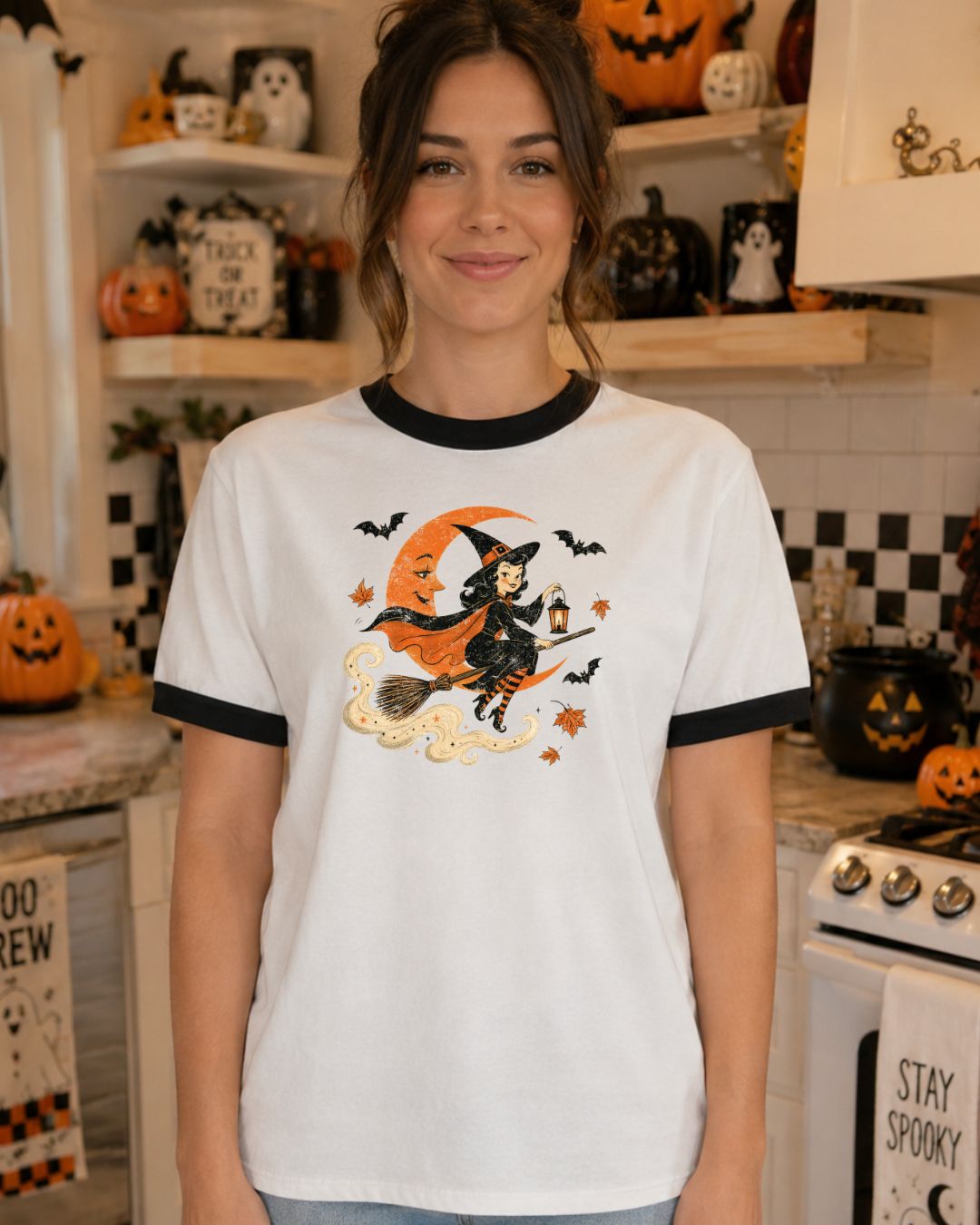 Woman wearing a white and black ringer tee with a vintage-style witch flying on a broomstick past an orange crescent moon with bats