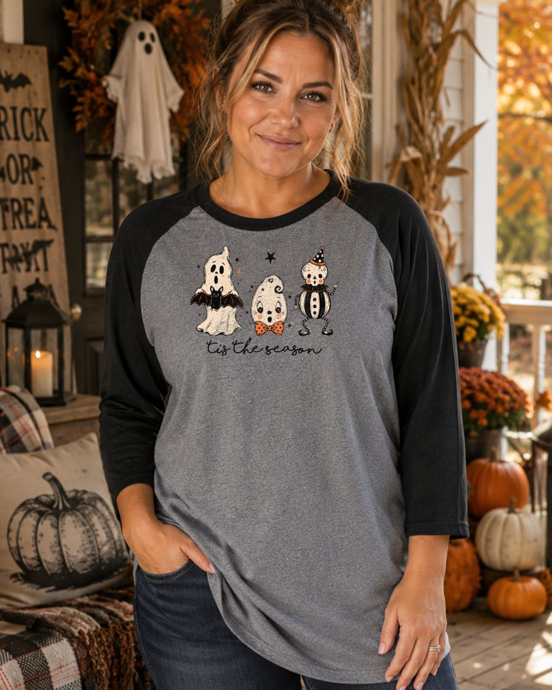 Woman wearing a grey and black raglan baseball tee with three Halloween ghost characters and "tis the season" script graphic