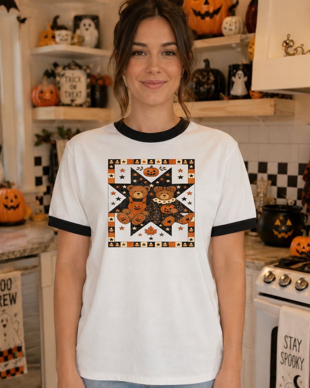Woman wearing a white and black ringer tee with a vintage quilt-style Halloween graphic featuring teddy bears, pumpkins, stars, and candy corn