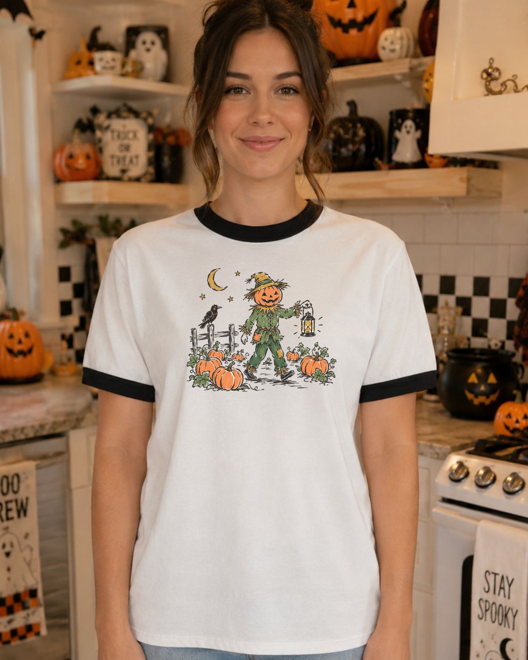 Woman wearing a white and black ringer tee with a vintage illustration of a pumpkin-headed scarecrow carrying a lantern through a moonlit pumpkin patch