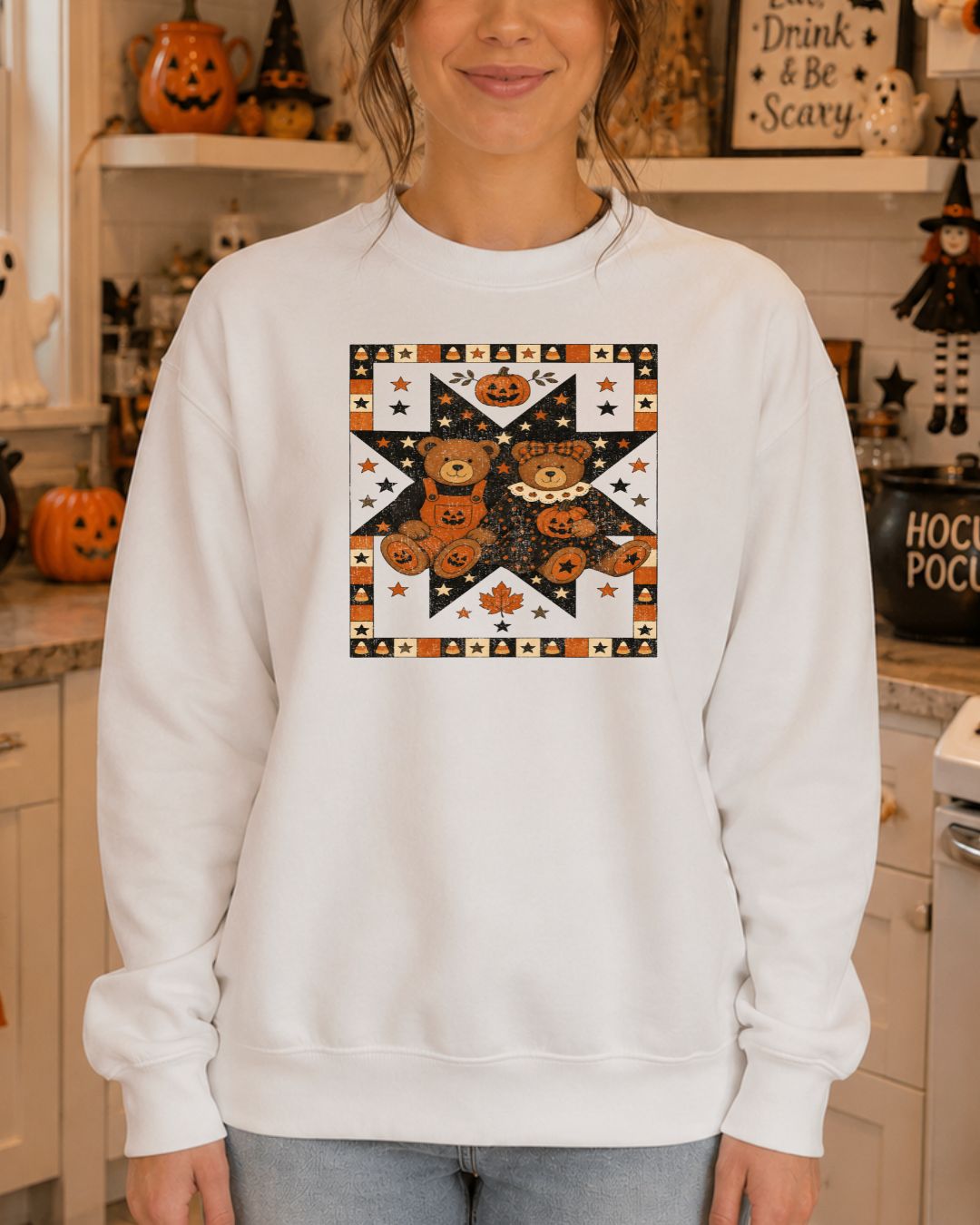 Woman wearing a white crewneck sweatshirt with a vintage quilt-style Halloween graphic featuring two teddy bears holding jack-o-lanterns surrounded by stars and candy corn