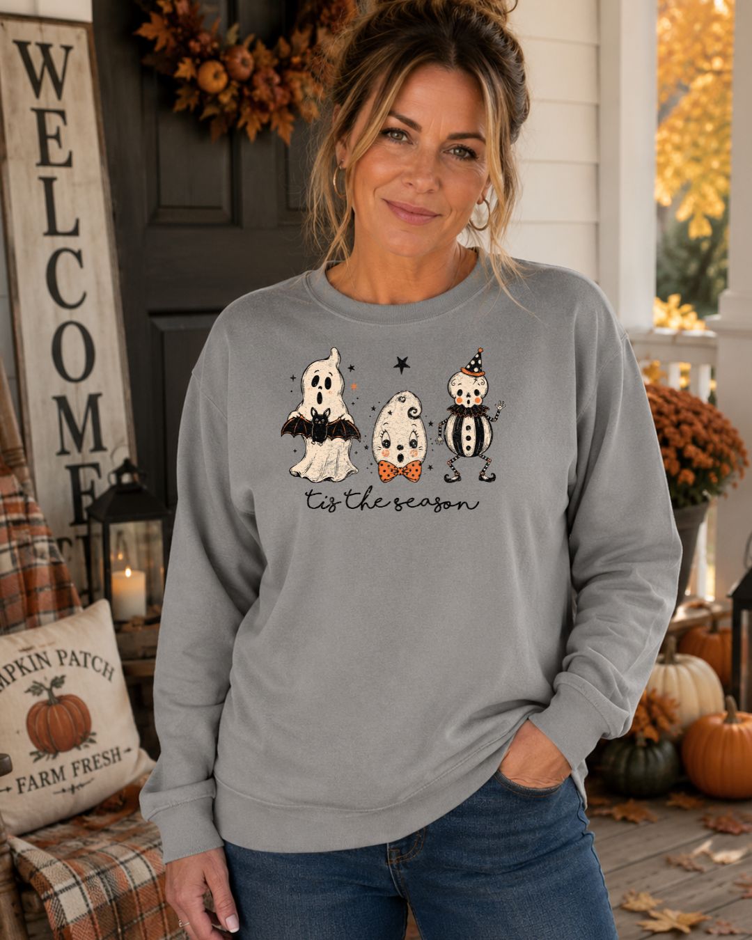 Woman wearing a grey crewneck sweatshirt with three Halloween ghost characters and "tis the season" script graphic
