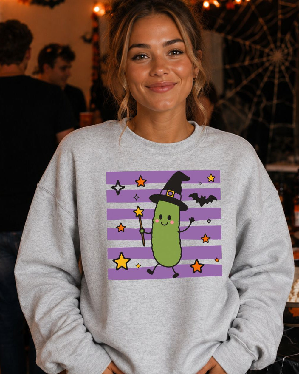 Witch Pickle Crewneck Sweatshirt in Ash Grey featuring a smiling pickle in a witch hat holding a wand on a purple striped background with stars and bats