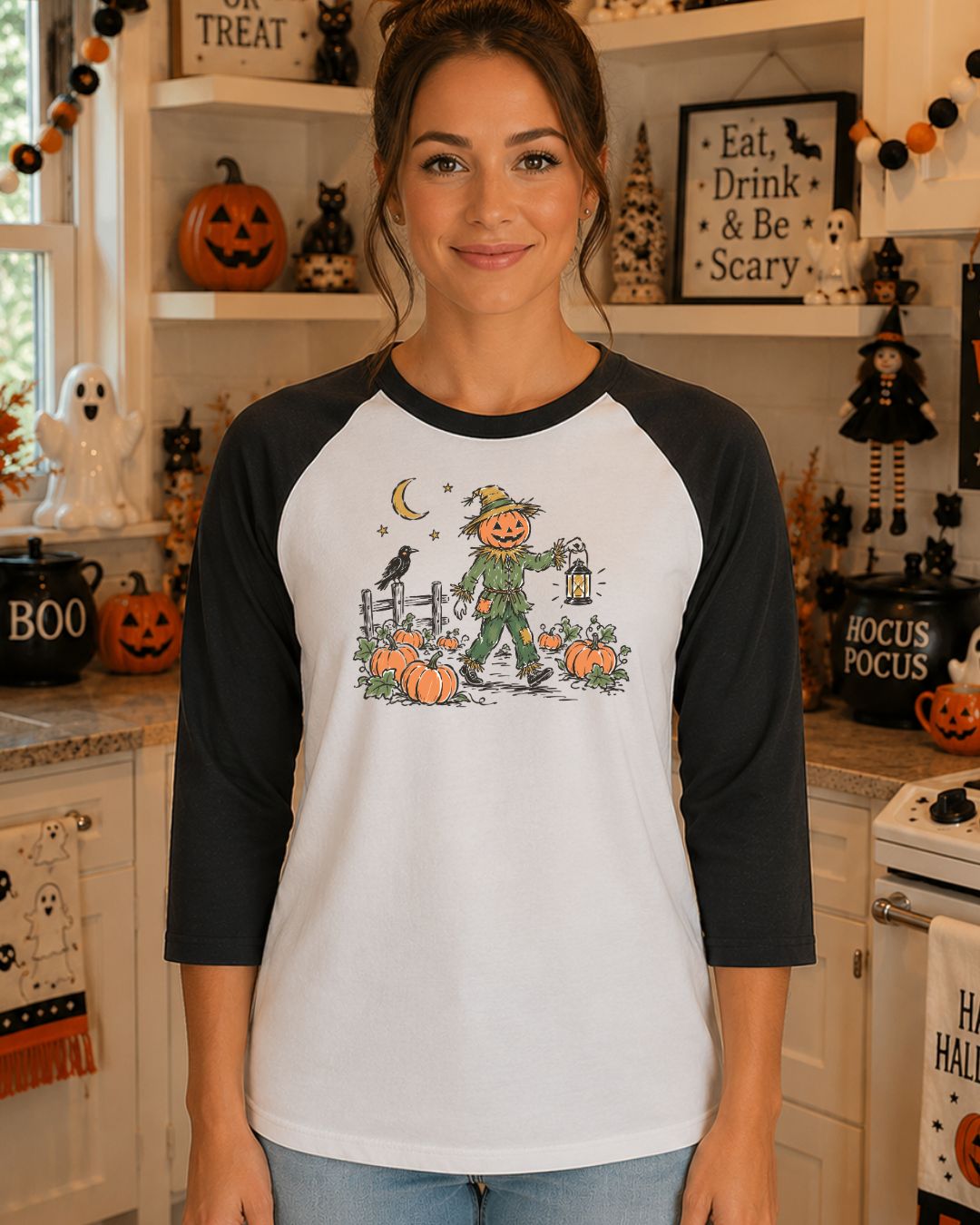 Woman wearing a white and black raglan baseball tee with a vintage illustration of a pumpkin-headed scarecrow carrying a lantern through a moonlit pumpkin patch with a crow on a fence post